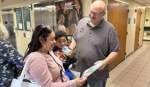Photo from University Health Professionals book giveaway in Hartford, Conn. A man and a woman look at a book while the woman holds a baby.