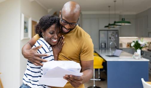 stock photo: black couple (male, female) hug while looking at a document