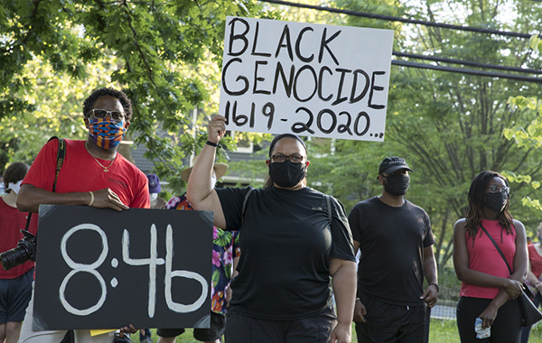 Protestors hold signs saying "8:46" and Black Genocide 1619-2020..."