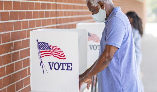 man in a mask votes at a voting booth