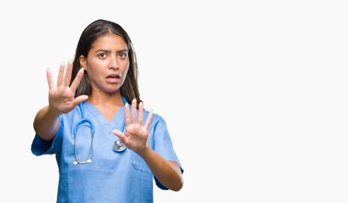 woman in scrubs holding up both of her hands in front of her as if to defend herself