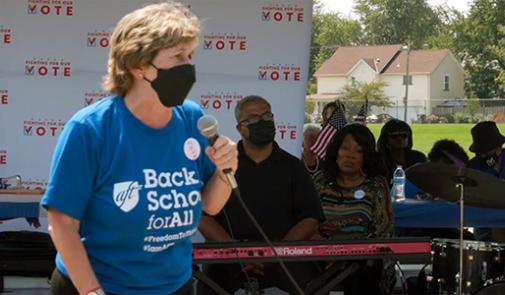 A woman, Randi Weingarten, holds a microphone at an event. She is wearing a mask covering her nose and mouth.