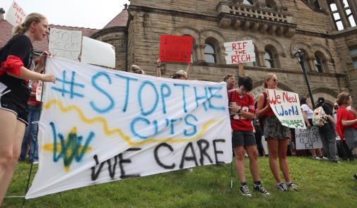 Estudiantes, profesores y empleados de la Universidad de West Virginia con carteles. El letrero en primer plano dice "#Stop the Cuts. We Care".