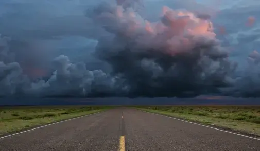 storm clouds in the distance over a long empty road
