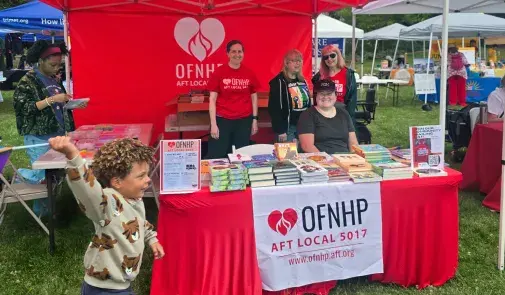 Young child with a Pride flag running in front of OFNHP booth at an outdoor event