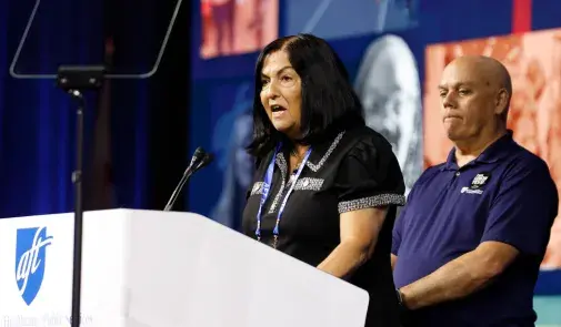 Anne Goldman stands at the podium with John Brady in the background.