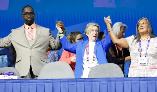 Re-elected officers Fedrick Ingram, Randi Weingarten and Evelyn DeJesus hold hands onstage.
