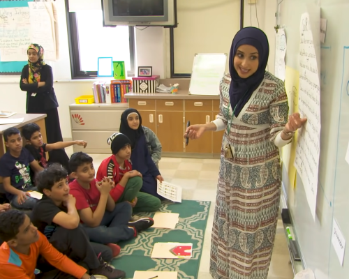 Still from You Are Welcome Here. A teacher is teaching in a classroom