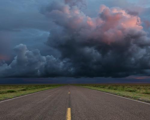 storm clouds in the distance over a long empty road
