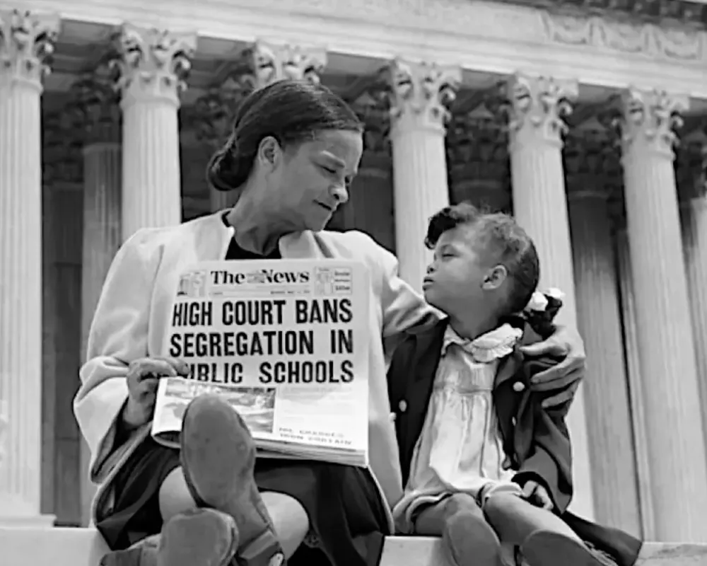 Nettie Hunt sits with her daughter on the steps of the Supreme Court. Newspaper reads "High Court Bans Segregation in Schools"