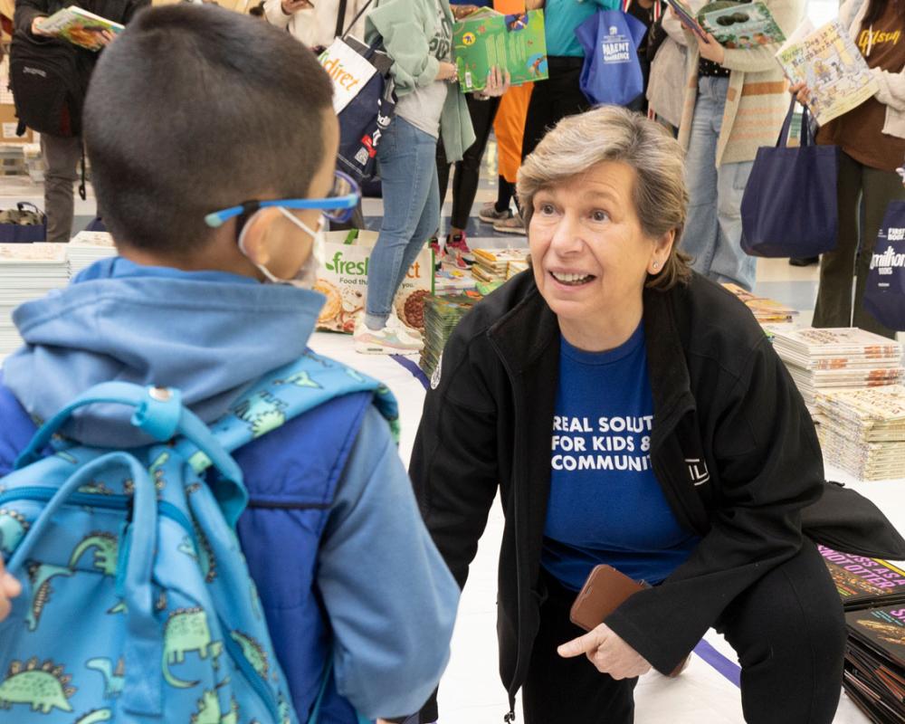 AFT President Randi Weingarten crouched to talk with a small child amid piles of free books