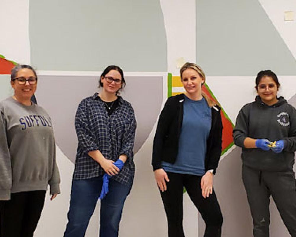 Trudy Christ, second from the right, poses in front of a painted painted wall with two of her students, two on her left and one on her right