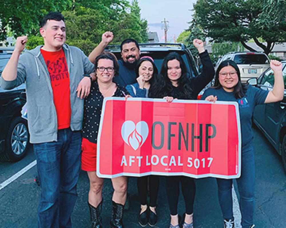 la gente se para con el puño en alto detrás de un cartel que dice "OFNHP AFT Local 5017"