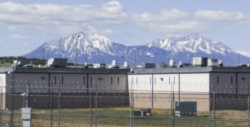 a picturesque scene of the Rocky Mountains behind a closed private prison