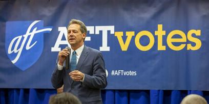 El gobernador Bullock habla frente a un cartel de 'votos AFT'