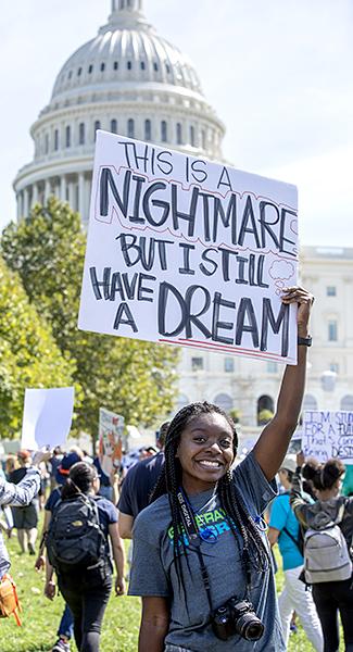 a girl holds a sign that says 'this is a nightmare but I still have a dream'