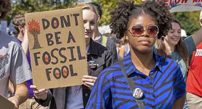 a young woman holds a sign that says 'don't be a fossil fool'