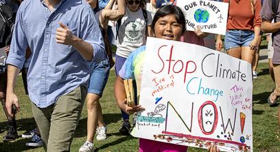 young girl holds a sign that says 'stop climate change now!'