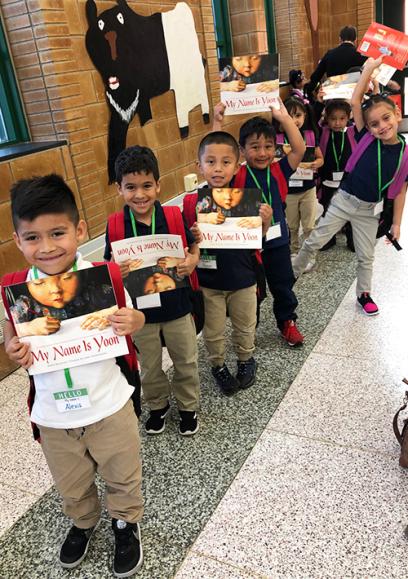 Una línea de pequeños niños latinos posan para una foto con sus libros. ellos están sonriendo.