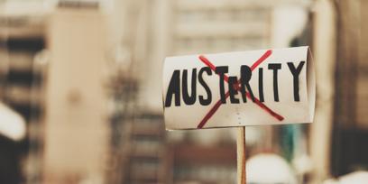 una señal de protesta tiene la palabra austeridad con una x roja sobre ella