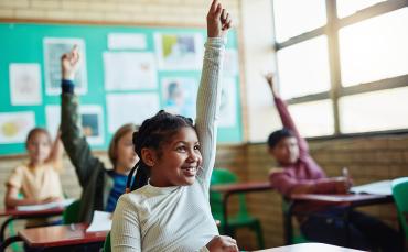 young black girl in foreground raises hand with smile on her face