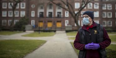 person in mask and gloves stand sin front of building