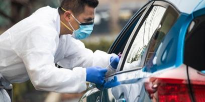 man in protective gear greets car at coronavirus testing site