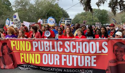 los educadores que protestan sostienen un cartel que dice que las escuelas públicas financian nuestro futuro