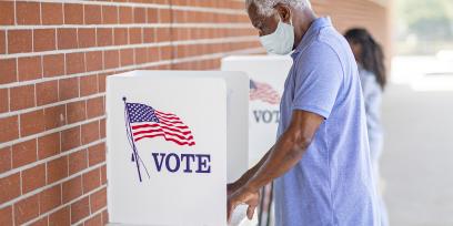 man in a mask votes at a voting booth