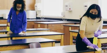 teachers with mask and gloves on disinfect desks