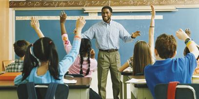 black teacher stands in front of his class. the children raise their hands