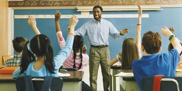 profesor negro se para frente a su clase. los niños levantan la mano