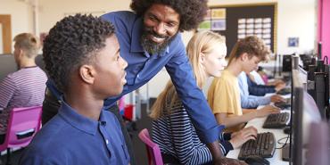 black teacher smiles and helps his black student