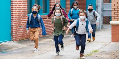 six children wearing masks and backpacks are running toward camera