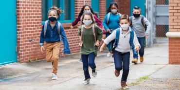 six children wearing masks and backpacks are running toward camera