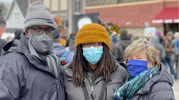 three people, Fed Ingram, Marcia Howard, and Randi Weingarten stand in George Floyd Square