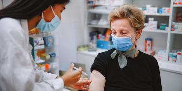 doctor giving woman vaccine. they both wear masks