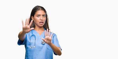 woman in scrubs holding up both of her hands in front of her as if to defend herself