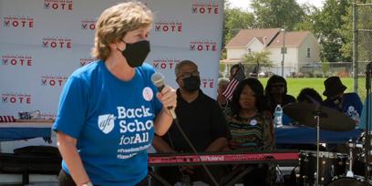 A woman, Randi Weingarten, holds a microphone at an event. She is wearing a mask covering her nose and mouth.