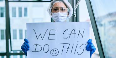 a healthcare work in ppe holds a sign that says we can do this