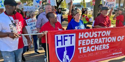 Foto del presidente de la AFT, Randi Weingarten, el presidente de la HFT, Jackie Anderson, y los miembros de la HFT marchando con una pancarta que dice "Maestros de la Federación de Houston". Local 2415 | EN POPA | TEXAS EN POPA | AFT-CIO"