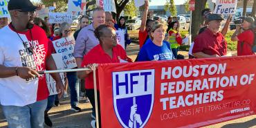 Foto del presidente de la AFT, Randi Weingarten, el presidente de la HFT, Jackie Anderson, y los miembros de la HFT marchando con una pancarta que dice "Maestros de la Federación de Houston". Local 2415 | EN POPA | TEXAS EN POPA | AFT-CIO"