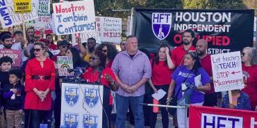 HFT President Jackie Anderson speaking at podium surrounded by HFT members and family members. To the right stands AFT Executive Vice-President Evelyn DeJesus