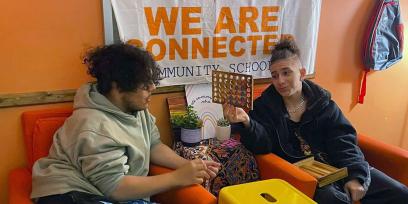 Foto de dos chicos hablando. Un cartel detrás de ellos dice "Estamos conectados. Escuela comunitaria".