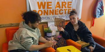 Foto de dos chicos hablando. Un cartel detrás de ellos dice "Estamos conectados. Escuela comunitaria".