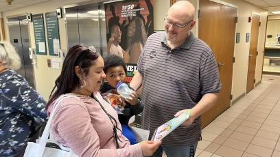 Photo from University Health Professionals book giveaway in Hartford, Conn. A man and a woman look at a book while the woman holds a baby.