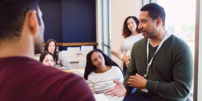 Black male college professor talks to diverse group of students in classroom