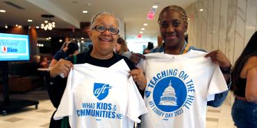 Foto de la maestra jubilada Teresa Reaves y la paraprofesional Tracy Romain del Boston Teachers Union sosteniendo camisetas que decían "What Kids & Communities Need" y "Teaching on the Hill. AFT Lobby Day 2023", respectivamente