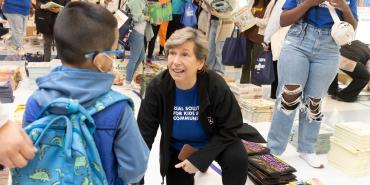 AFT President Randi Weingarten crouched to talk with a small child amid piles of free books