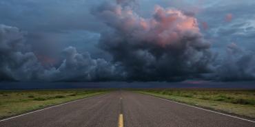 storm clouds in the distance over a long empty road